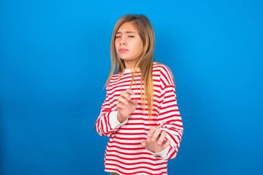 Ne kadar iğrenç! Mavi arka planda çizgili tişört giyen hoşnutsuz genç kız, iğrenç bir şey gördüğü için tatminsiz yüz ifadesi sergiliyor..