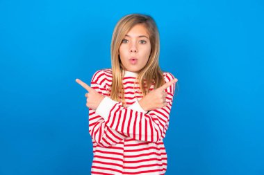 Kafası karışmış, mavi arka plan üzerinde çizgili tişört giyen güzel beyaz kız iki taraf arasında seçim yapıyor, iki tarafı da çapraz ellerle işaret ediyor, şüphe duyuyor. Tavsiyene ihtiyacım var..