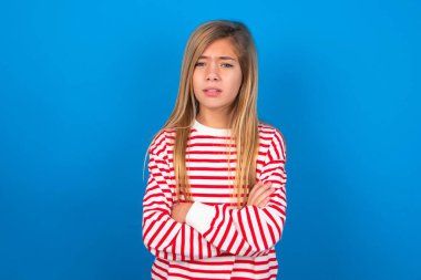 Mavi arka planda çizgili tişört giyen genç kız hoşnutsuzca kaşlarını çatmış, kollarını kavuşturmuş, bir açıklama bekliyor..