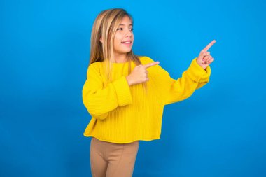 Mavi arka planda sarı süveter giyen güzel beyaz kız gülümseyerek parmaklarını yönetiyor. 