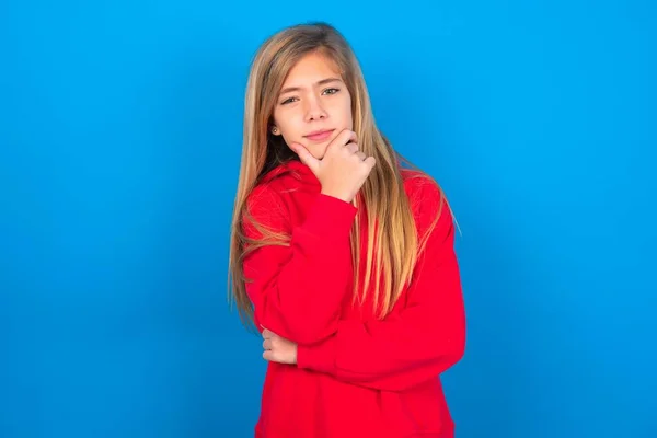 Nachdenkliches Kaukasisches Teenie Mädchen Rotem Sweatshirt Vor Blauem Hintergrund Hält — Stockfoto