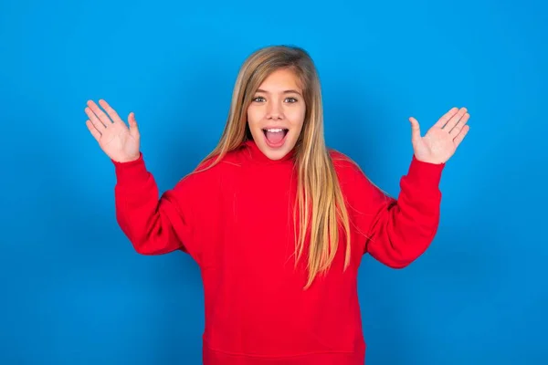 青い背景に赤いスウェットシャツを着て美しい慎重な十代の少女は 彼女の偉大な業績を喜んで幸せに満ちた目を持っています 成功コンセプト — ストック写真