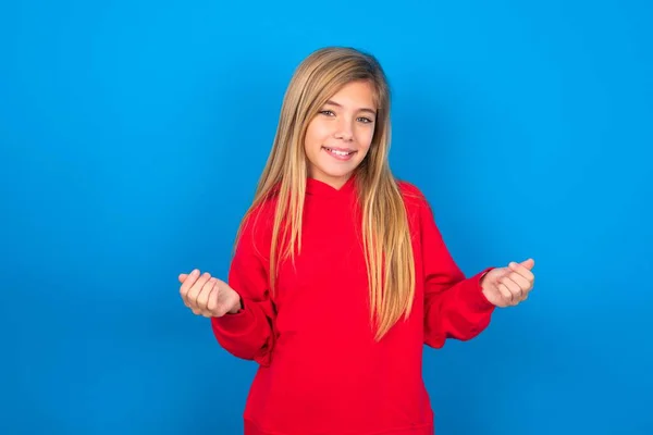 お金のジェスチャーを作る青い背景に赤いスウェットシャツを着ている美しい慎重な十代の少女 — ストック写真