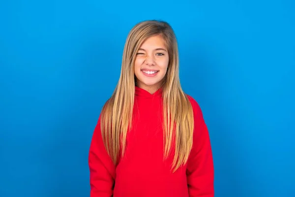 美しい慎重な十代の少女は 幸せな表情を持つ喜びで青い背景に赤いスウェットシャツを着ています フェイシャル表現と人々の感情コンセプト — ストック写真