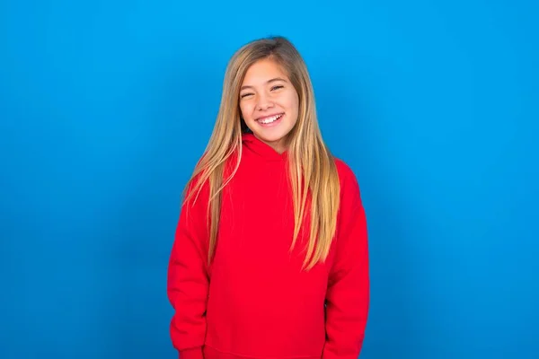青い背景に赤いスウェットシャツを着ている笑顔の慎重な十代の少女は白い歯を示し 自信を持って休む喜びを感じます — ストック写真