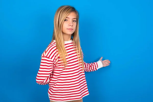 歓迎のジェスチャーでアームアウトブルーの背景にストライプのシャツを着ている10代の少女の肖像画 — ストック写真