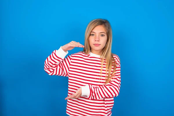 青い背景のジェスチャー上のストライプシャツを身に着けている十代の少女は 大きなと大きなサイズのサインを示す手で シンボルを測定します — ストック写真