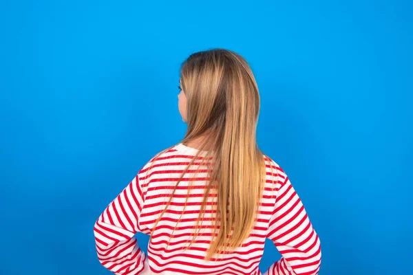 青いスタジオの背景に青い背景の上にストライプのシャツを着ているブロンドの十代の少女の背中の景色 — ストック写真