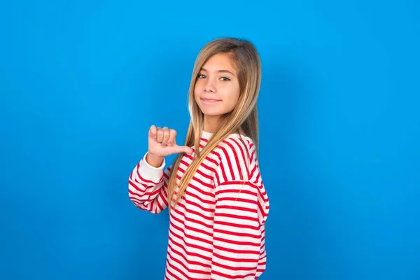 青い背景の上にストライプシャツを着ている陽気な十代の少女のクローズアップは喜び 満足し 自信を持って見えます 親指で自分自身を指します — ストック写真