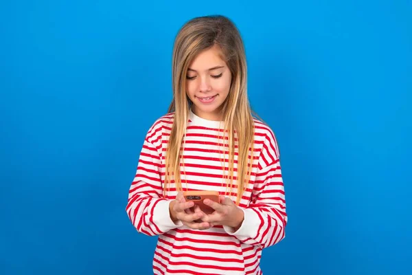 Uśmiechnięta Nastolatka Nosząca Koszulę Paski Niebieskim Tle Korzystająca Telefonu Komórkowego — Zdjęcie stockowe