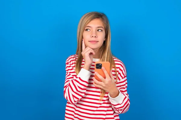 夢を見ている10代の少女は 携帯電話を使用して青い背景にストライプのシャツを着て 顔に手を握ります 意思決定とソーシャルメディアのコンセプト — ストック写真
