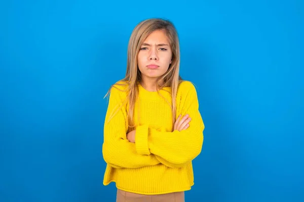 青いスタジオの背景に黄色いセーターを着用している不満の白人十代の少女は額の下からカメラで悲惨な表情で 不幸な悲しみを作ります — ストック写真