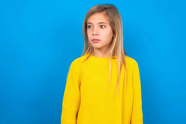 青いスタジオの背景の上に黄色いセーターを着ている美しい白人の十代の少女は 不思議な表情を持っています 恥ずかしいモデルがサプライズに見える — ストック写真