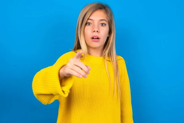 惊慌失措的高加索少女穿着黄色毛衣站在蓝色工作室的背景点上 带着惊讶的表情看着你 — 图库照片
