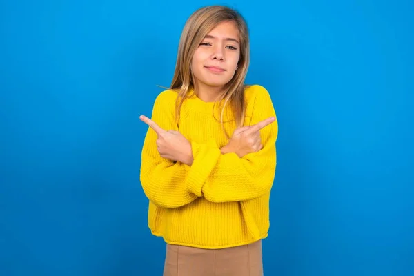 파란색 스튜디오 배경에 노란색 스웨터를 코카서스 소녀는 포인트를 결정에 도움이 — 스톡 사진