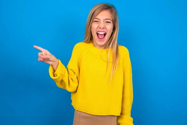 笑着在蓝色工作室背景点上穿黄色毛衣的高加索少女 在复制的空白空间旁边 人的促销和广告概念 — 图库照片