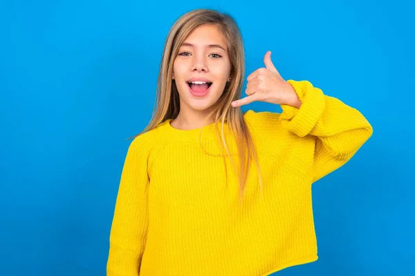 青いスタジオの背景に黄色いセーターを着ている美しい白人十代の少女は電話のジェスチャーを作ります 私を再度呼び出すと言います 喜びの表現を持っています — ストック写真