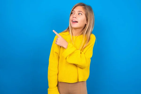 青いスタジオの背景に黄色いセーターを着てコピースペースを示すラグジュアリーな十代の少女 — ストック写真