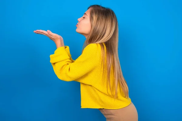 青いスタジオの背景に黄色のセーターを着ている美しい白人十代の少女のプロフィールの側面のビューの肖像画 — ストック写真