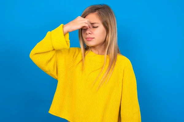 悲しい慎重な十代の少女は 頭痛に苦しむ青いスタジオの背景に黄色いセーターを着て 彼女の顔に手を握っています — ストック写真