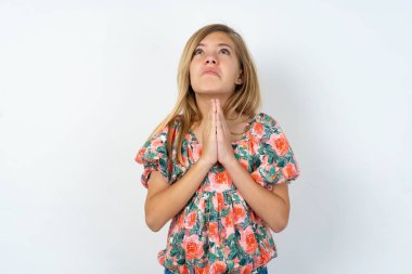 Beyaz duvarın üzerinden çiçekli bluz giyen güzel beyaz kız elleri bağlı yalvarıyor ve dua ediyor. Yüzünde umut ifadesi var. Çok duygusal ve endişeli. Lütfen Tanrım.