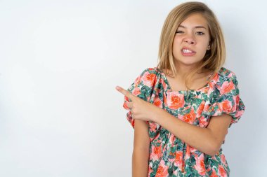 Beyaz duvarın üzerinden çiçekli bluz giyen güzel beyaz kız işaret parmağı, endişe ve sürpriz konseptiyle endişeli ve gergin..