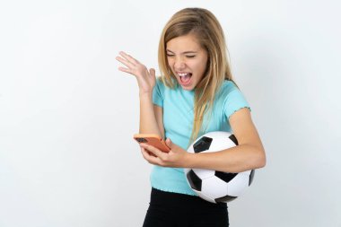 Kızgın, beyaz, beyaz, beyaz bir duvarın üzerinde futbol topu tutan beyaz giysili genç kız telefonda bağırıyor. İşte sorunlar var.. 