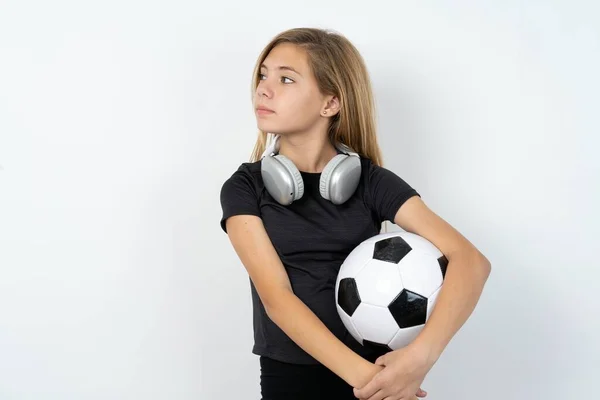 身穿运动服 头戴足球球衣 头戴白色墙壁的少女高兴地把双手交叉在胸前看向一边 — 图库照片
