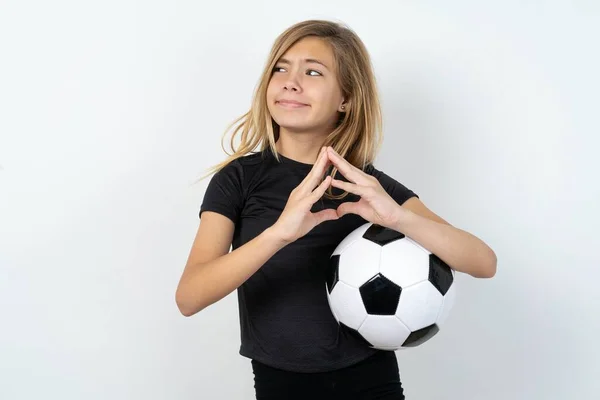 ホワイトウォールの指の上にサッカーボールを持っているスポーツウェアを身に着けているティーンガールは ミステリアスに見えますが 大きな邪悪な計画を念頭に置いて — ストック写真