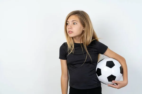 身穿运动服 头戴足球球衣 头戴白色墙壁的少女 带着惊奇的表情凝视着旁边 她的表情说不出话来 尴尬的模型看上去很惊讶 — 图库照片