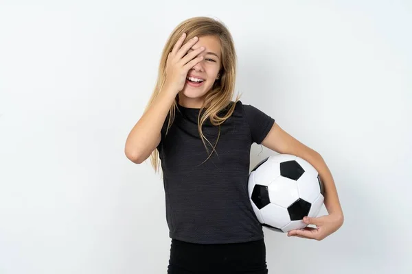 身穿运动服的少女拿着足球冲过白墙 满脸笑容 笑着肯定听到滑稽的笑话 — 图库照片