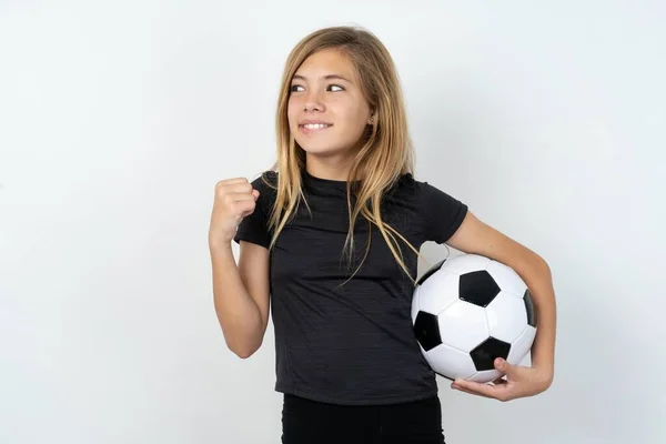 身穿运动服的少女拿着足球穿过白墙紧紧抓住拳头 等待着美好的事情发生 — 图库照片
