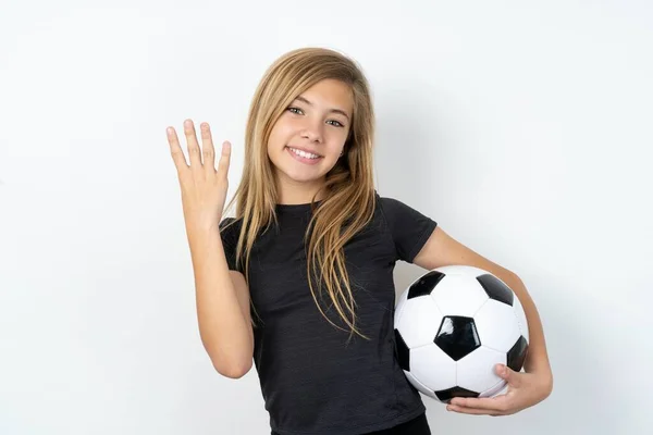 ホワイトウォールの上にサッカーボールを保持し 笑顔でフレンドリーに見えるスポーツウェアを着ているティーンガールは 4番目または4番手を前方に表示し カウントダウン — ストック写真