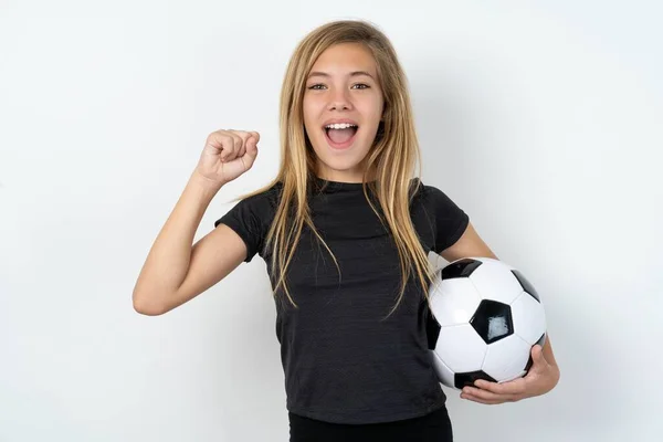 惊喜交集身穿运动服的少女拿着足球冲过白墙赢了彩票举手欢呼耶 — 图库照片