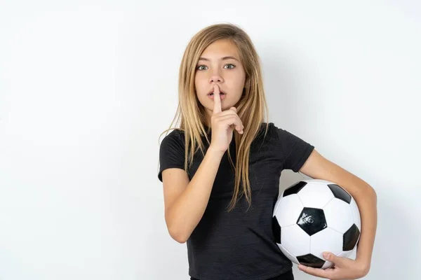 身穿运动服 头戴足球球衣 头戴白色墙壁的少女惊讶地做出沉默的姿态 用手指捂住嘴唇 在镜头前显得神秘而神秘 — 图库照片