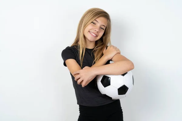 ホワイトウォールの上にサッカーボールを保持するスポーツウェアを着用する魅力的な10代の少女は 快適なポーズを感じます 緊張と自尊心の概念 — ストック写真