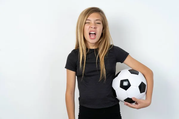 身穿运动服的少女拿着足球在白墙上打呵欠 张大了嘴 每天早上的例行公事 — 图库照片