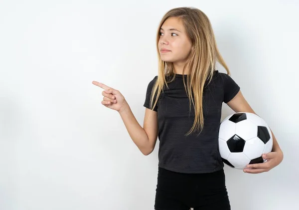 コピースペースでホワイトウォールポイントの上にサッカーボールを保持するスポーツウェアを着てティーンガール 何かを宣伝 アドバイス最高の価格 — ストック写真