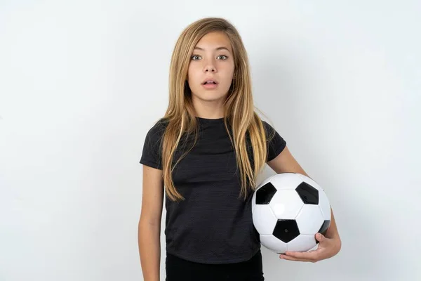 白い壁の星の上にサッカーボールを保持するスポーツウェアを身に着けているショックを受けたティーンガールは 口を開いたままの目は驚きの表情をしています Omgコンセプト — ストック写真