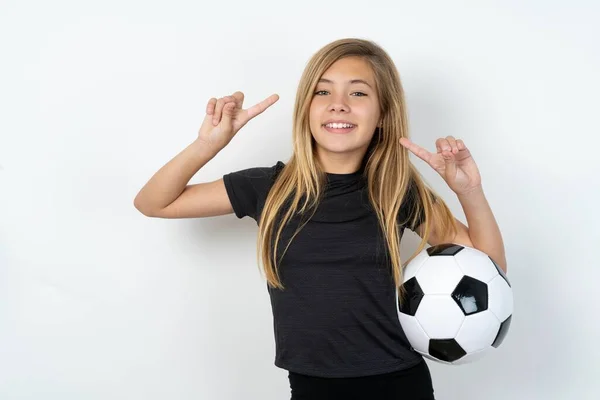身穿运动服的快乐少女拿着足球在白墙上展示自己的发型 — 图库照片
