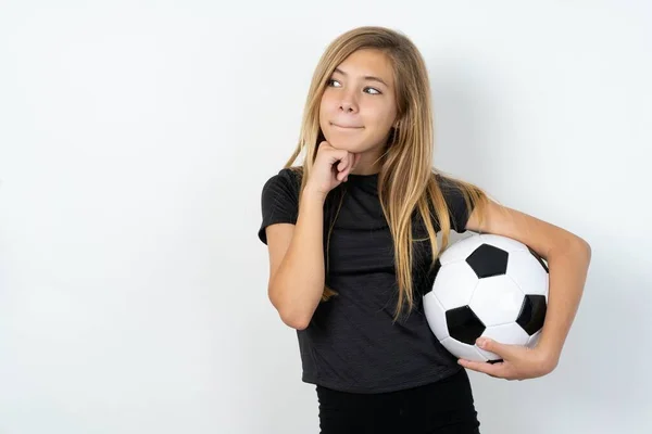 Любопытная Девочка Спортивной Одежде Держит Футбольный Мяч Над Белой Стеной — стоковое фото