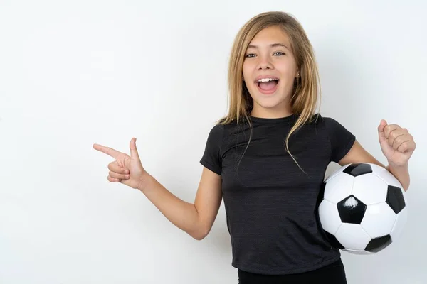 ホワイトウォールポイントの上にサッカーボールを保持するスポーツウェアを着ている十代の少女は 拳を握る空の空間で 勝者のジェスチャー — ストック写真