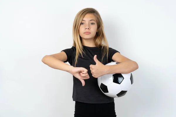 サッカーボールをホワイトウォールの上に保持するスポーツウェアを着ているティーンガールは サインアップサインを示しています — ストック写真