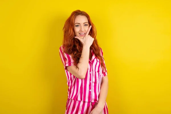 黄色いスタジオの背景にピンクのピンクのパジャマを身に着けている若い赤毛の女性は 交差した腕と手で笑っているカメラに自信を持って見ています ポジティブに考える — ストック写真