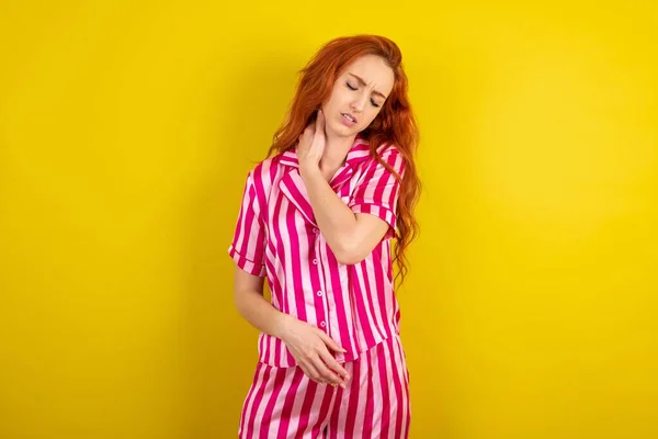 Jonge Roodharige Vrouw Draagt Roze Pyjama Gele Studioachtergrond Heeft Nekpijn — Stockfoto