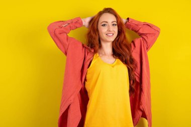 Güzel kızıl saçlı kadın sarı stüdyo arka planında duruyor, kollarını açıyor, rahat pozisyonda..