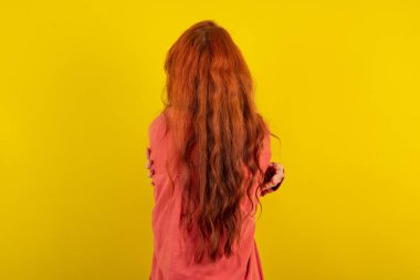 Güzel kızıl saçlı kadın sarı stüdyo arka planında dikiliyor mutlu ve pozitif bir şekilde kendini kucaklıyor. Sevgi ve özgüven.