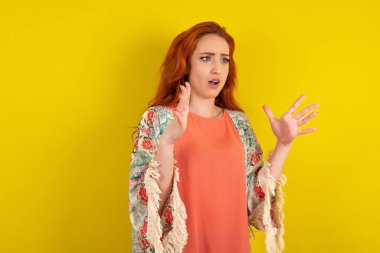 Sarı stüdyo arkasında duran kızıl saçlı kadın yüksek sesle bağırıyor, gözleri açık ve elleri gergin tutuyor..