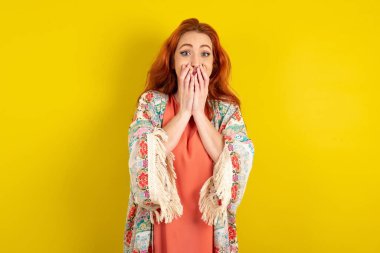 Sarı stüdyo arka planında duran neşeli kızıl saçlı kadın, neşe içinde kıkırdıyor, ağzını kapatıyor, doğal kahkahalar atıyor, olumlu hikayeler dinliyor ya da komik anekdotlar dinliyor.