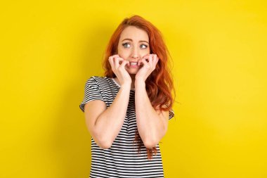 Sarı arka planda çizgili tişört giyen kızıl saçlı kadın boş bir uzay evi gibi görünüyor.